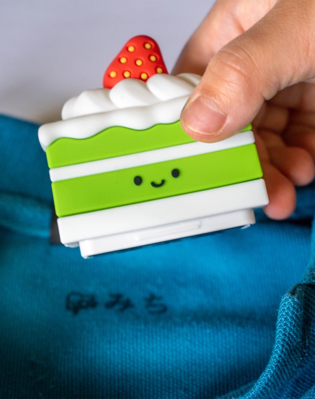 Fingers holding onto the Cake-licious name stamp with blue clothing in the background showing an imprint